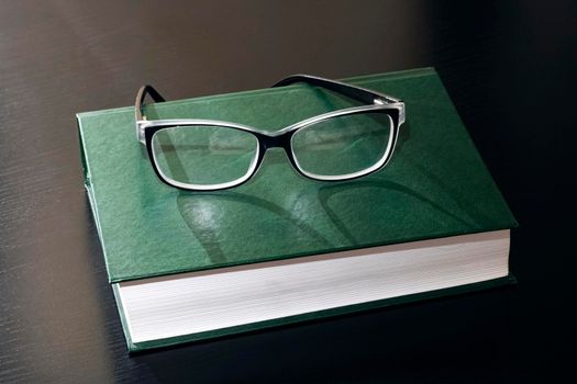 Black glasses on a book on a wooden table close up