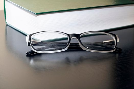 Black glasses and a book on a wooden table close up