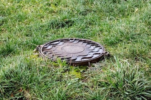 Sewer manhole among green grass close up in summer