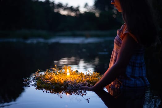 Young girl holding wreath with burning candle, setting it to flow on the river, making a wish