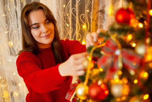 Festive warm atmosphere of a young girl hanging baubles to christmas tree