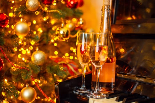 Bottle of white wine and two wineglasses full of drink on the piano with background of Christmas tree