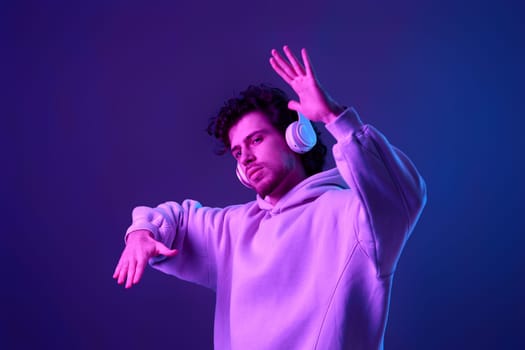 handsome bearded man with headphones in sweatshirt enjoying favorite music on blue background. Neon lighting