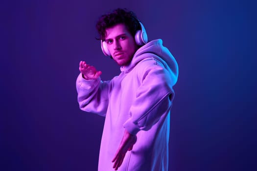 handsome man with headphones in sweatshirt enjoying favorite music on blue background. Neon lighting