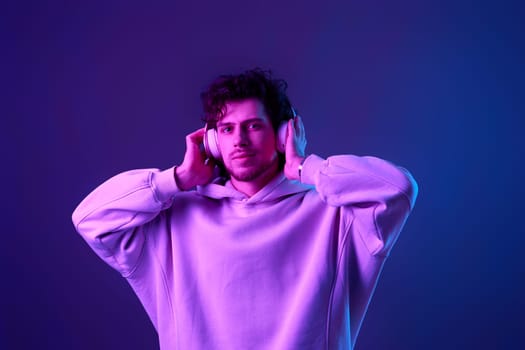 handsome man listening to music with wireless headphones on blue background. Neon lighting