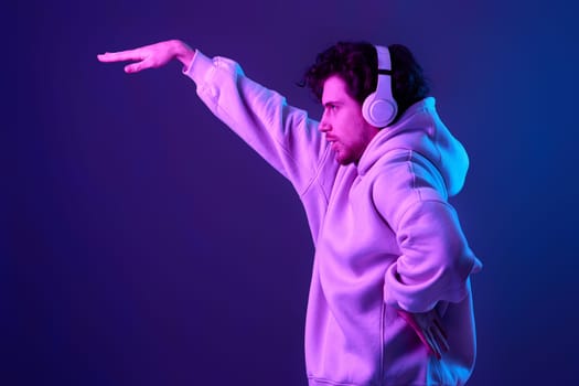 handsome man with headphones in sweatshirt enjoying favorite tracks on blue background. Neon lighting