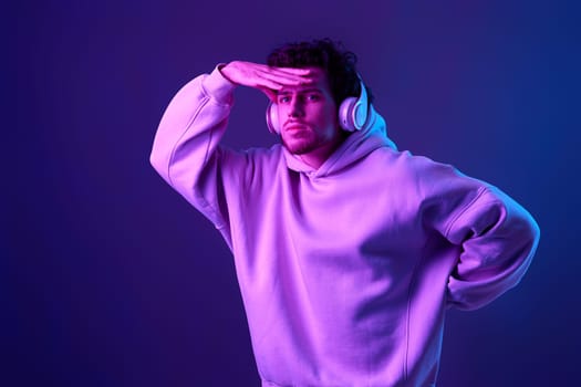 handsome man with headphones in sweatshirt enjoying favorite tracks on blue background. Neon lighting