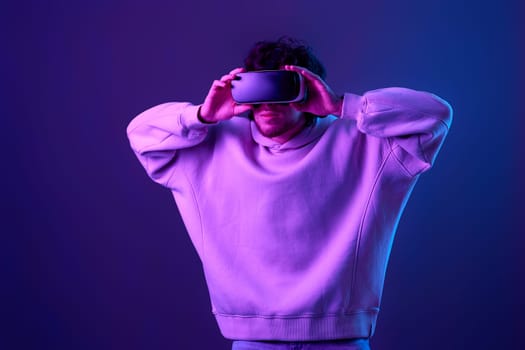 man in sweatshirt using virtual reality glasses on blue background. Neon lighting