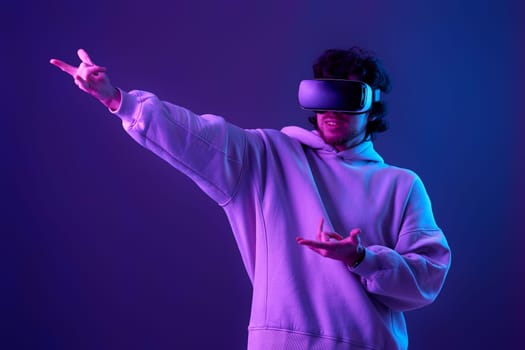 man in sweatshirt using virtual reality headset on blue background. Neon lighting