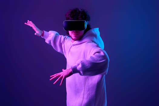 man in vr glasses and sweatshirt plays and tries to touch something on blue background. Neon lighting