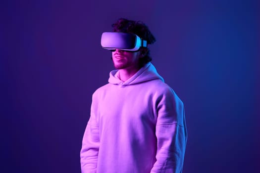 man in sweatshirt using virtual reality glasses on blue background. Neon lighting