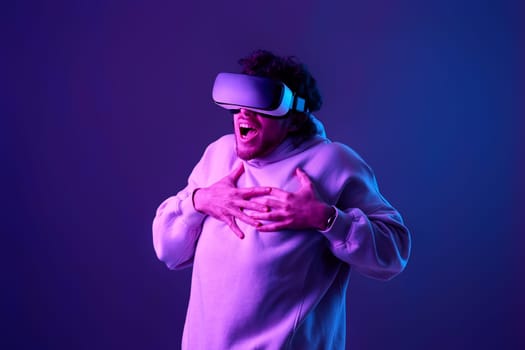 man in sweatshirt using virtual reality glasses on blue background. Neon lighting