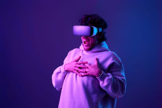 man in sweatshirt using virtual reality glasses on blue background. Neon lighting