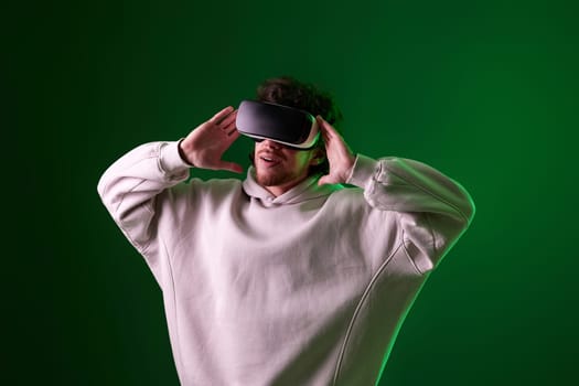 man in sweatshirt using virtual reality headset on green background. Neon lighting