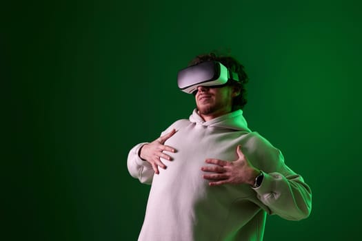 man in sweatshirt using virtual reality headset on green background. Neon lighting