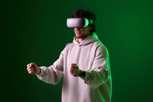 man in sweatshirt using virtual reality headset and playing video games on green background. Neon lighting