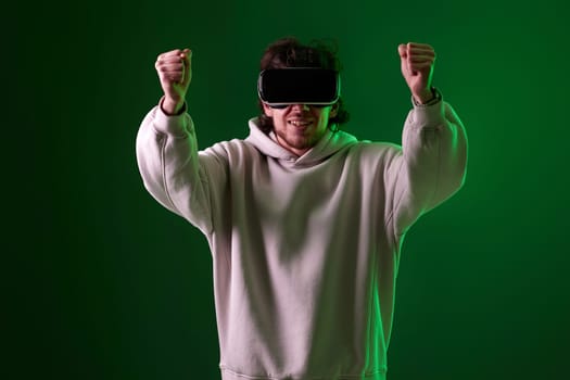 man in sweatshirt using virtual reality headset on green background. Neon lighting