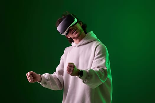 man in sweatshirt using virtual reality headset on green background. Neon lighting