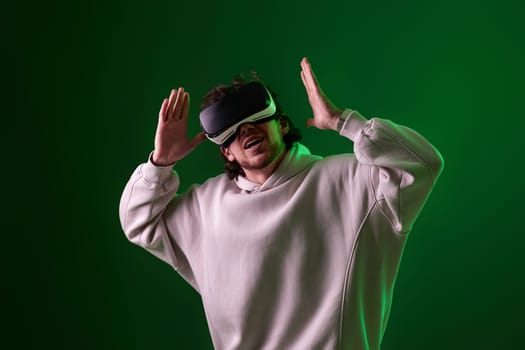 man in sweatshirt using virtual reality headset on green background. Neon lighting