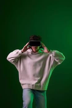 man in sweatshirt using virtual reality headset on green background. Neon lighting