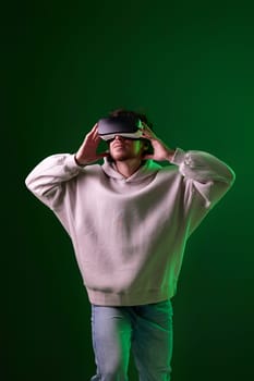 man in sweatshirt using virtual reality headset on green background. Neon lighting