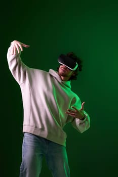 man in vr glasses and sweatshirt playing video games with his friends on green background. Neon lighting