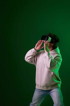 man in sweatshirt using virtual reality headset on green background. Neon lighting