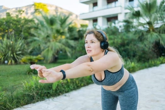 Adorable fat woman in tracksuit is engaged in fitness outdoor side view portrait. Young overweight woman lunges outdoors on warm summer day. Healthy lifestyle and weight loss.