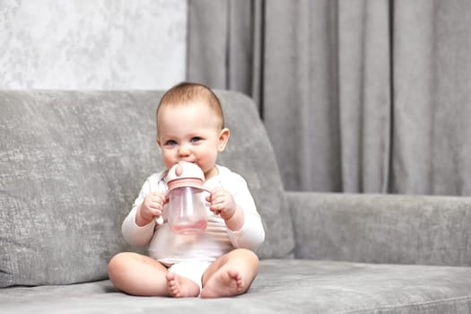 cute baby girl holding bottle and drinking water at home.