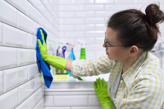 Woman housewife doing house cleaning in bathroom. Female polishing tiled wall in bathroom with microfiber cloth