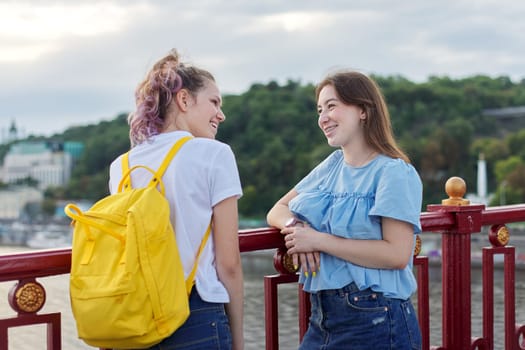 Portrait of two teenage girls standing on bridge over river, friends walk on summer sunny day. Friendship, lifestyle, youth, teens