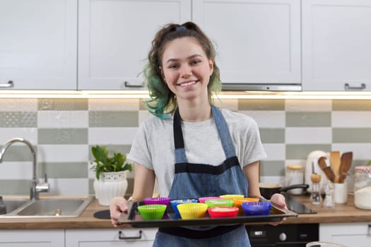 girl in apron in kitchen with tray of preparing raw silicone cupcakes. Home cooking, homemade food