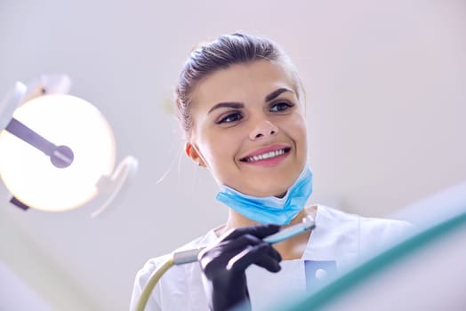 Female dentist treating teeth to patient, close-up face of doctor in mask with healing tools, copy space
