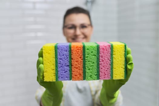 House cleaning concept. Woman in protective gloves holding many cleaning sponges, background bathroom interior, white ceramic tile