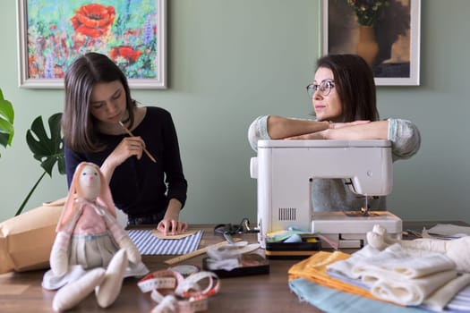 Mother and teen daughter sew together at home. Mom teaching daughter sewing on machine, women sew toy and clothes for toy. Parent and teenager, relationships, lifestyle, creativity, skill