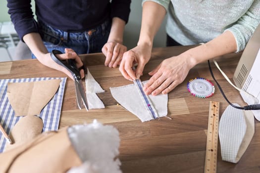 Sewing process close-up. Hands of woman and daughter of teenager child sewing toy doll clothes, with scissors, templates, needle, pattern, fabric, sewing machine