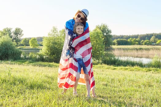 Happy mother and daughter child girl hugging under the American flag, USA, 4th of July, summer nature background