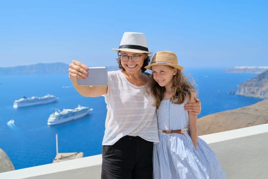Happy beautiful family, mother and little daughter traveling together in Mediterranean. Taking selfie using smartphone, beautiful scenic landscape with cruise liners background, copy space