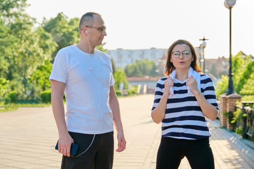 Couple of adult people resting talking after sports exercises, jogging in the park. Active healthy lifestyle, sport, fitness in middle-aged people