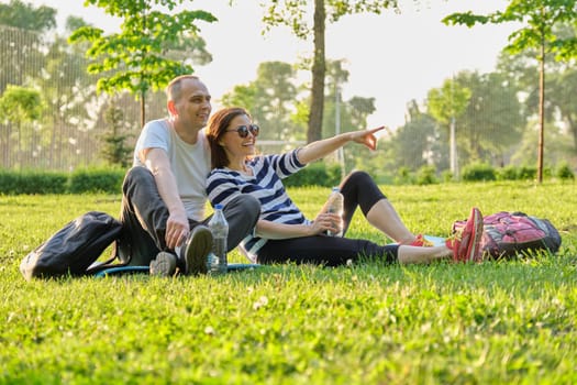 Middle-aged couple sitting on yoga mat, man and woman talking relaxing drinking water. Active healthy lifestyle, relationship, sport, fitness in mature people
