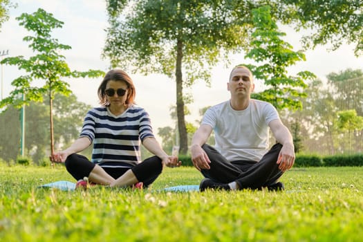 Couple, man and woman sitting in park on mat in lotus position and meditating. Yoga, fitness, active healthy lifestyle in middle-aged people