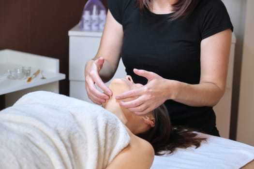 Professional facial massage, spa, beauty, face concept. Middle-aged woman receiving anti-aging massage, treatment in clinic