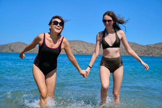 Mother teen daughter daughter together on the beach, walking by the sea in swimsuit, holding hands. Family vacations, summer holidays, communication, friendship, lifestyle, leisure, family