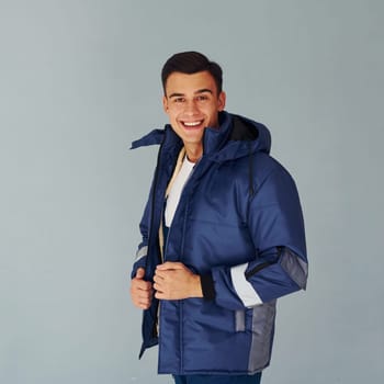 In warm jacket. Male worker in blue uniform standing inside of studio against white background.