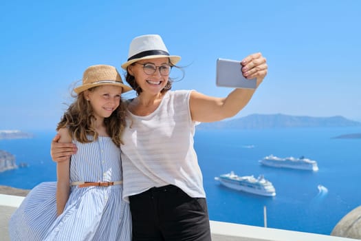 Happy beautiful family, mother and little daughter traveling together in Mediterranean. Taking selfie using smartphone, beautiful scenic landscape with cruise liners background, copy space
