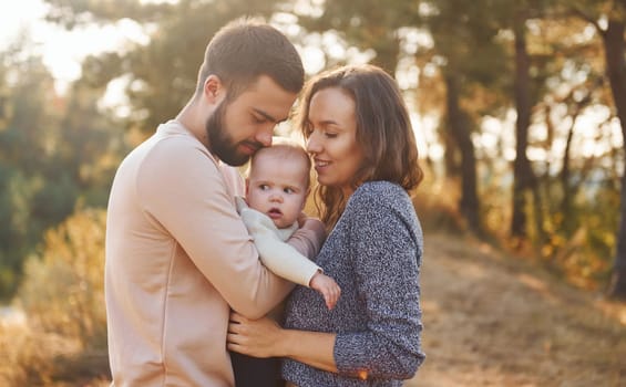 Happy family of mother, family and little baby rests outdoors. Beautiful sunny autumn nature.