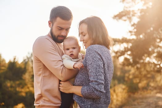 Happy family of mother, family and little baby rests outdoors. Beautiful sunny autumn nature.