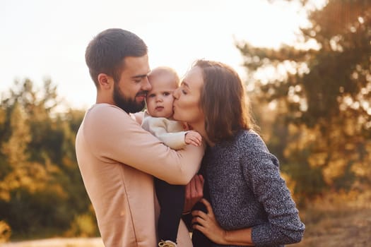 Happy family of mother, family and little baby rests outdoors. Beautiful sunny autumn nature.