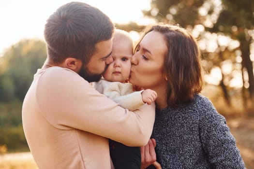 Happy family of mother, family and little baby rests outdoors. Beautiful sunny autumn nature.