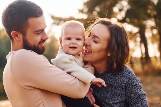 Happy family of mother, family and little baby rests outdoors. Beautiful sunny autumn nature.